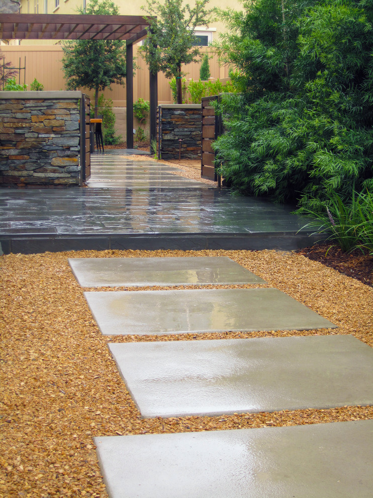 Entry with modular concrete pavers in decorative gravel leading to a blue stone landing patio. Podocarpus as the screening elements to cover adjacent home.
