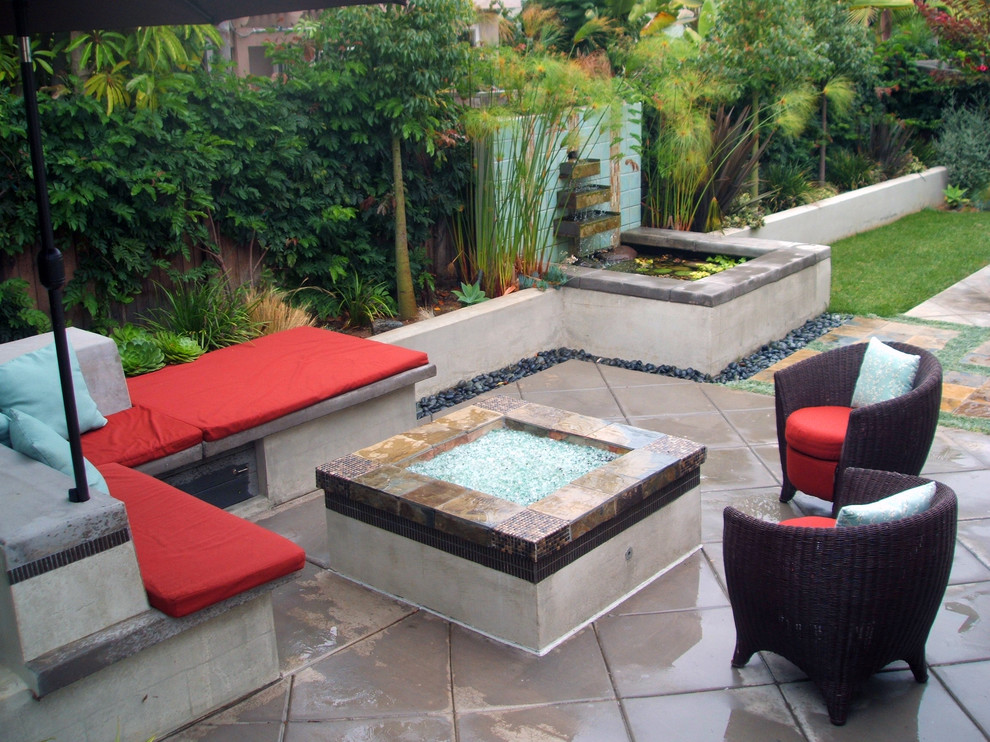 Built-in concrete bench with colorful cushions and accent pillows. Accent tiles with slate cap. Papyrus in foreground frames the intimate seating area with custom fire pit.